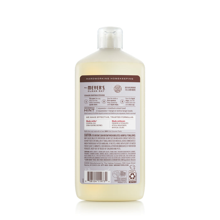 The back of a Mrs. Meyers Ultra Concentrated Liquid Laundry bottle displays product info and usage tips on an off-white background with brown/red text, emphasizing its garden scent. Recycling icons and tips can be found at the bottom.