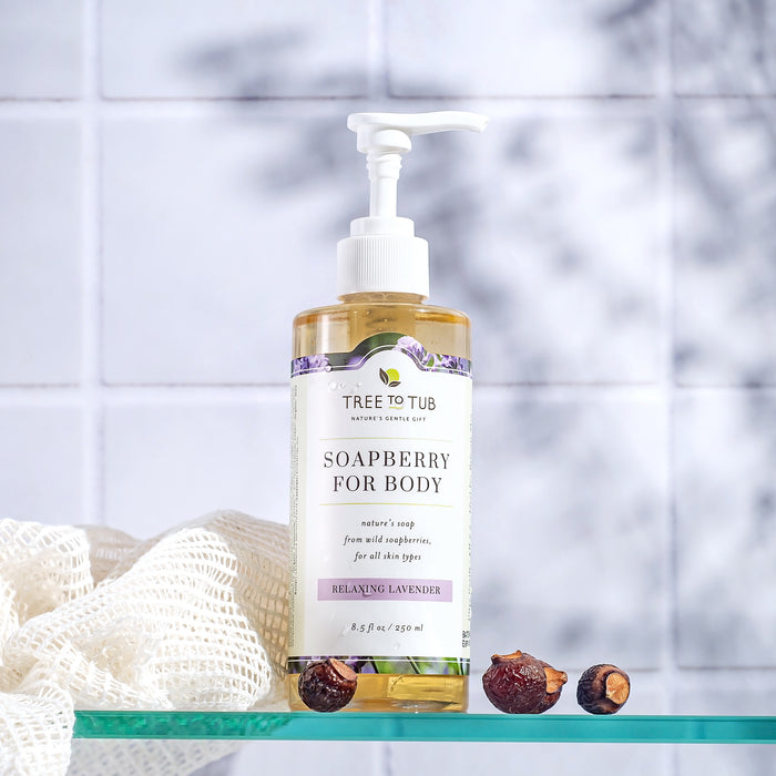 Tree To Tubs Ultra Hydrating Body Wash for Dry Skin in Relaxing Lavender scent rests on a glass shelf against white tiles, accompanied by a woven cloth and dried soapberries.