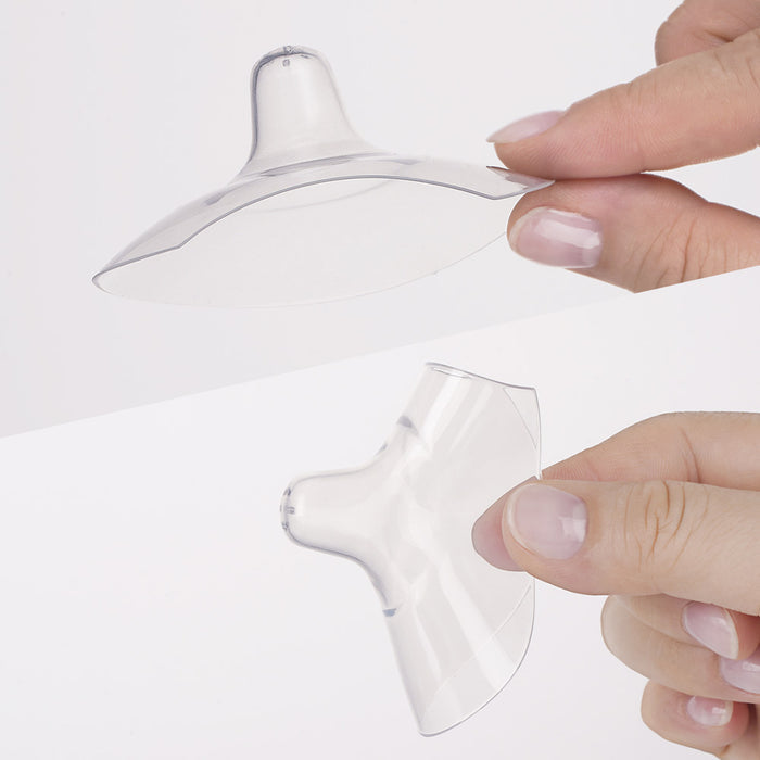 Two hands hold Haakaa Ultra-Thin Silicone Nipple Shields against a white background, showcasing their flexible, dome-shaped design. These transparent shields (Size M, 18mm) provide breastfeeding relief for sore nipples.