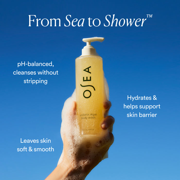 A hand covered in suds holds OSEA's Undaria Algae™ Body Wash against a clear blue sky. The text promotes hydration, skin barrier support, and reveals how it helps leave skin soft and smooth.