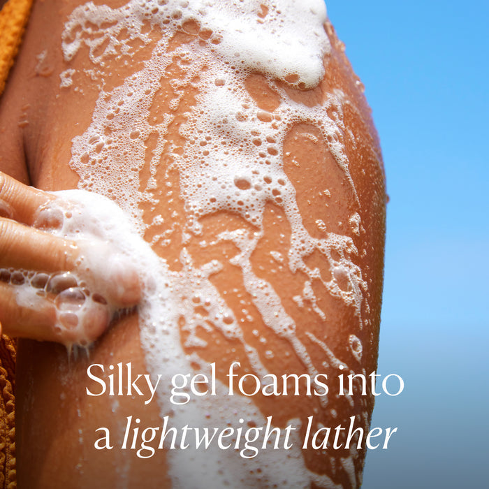A close-up of a shoulder and arm covered in foamy gel, with fingers gently lathering. Against a blue sky, white text reads: OSEA Undaria Algae™ Body Wash creates a silky, lightweight, pH-balanced foam.