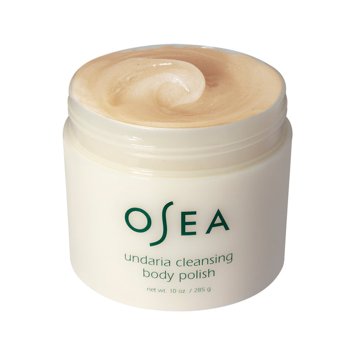 A jar of OSEAs Undaria Cleansing Body Polish contains a beige scrub with Undaria seaweed. The gel-to-milk body polish is labeled with its name and net weight of 10 oz / 285 g.