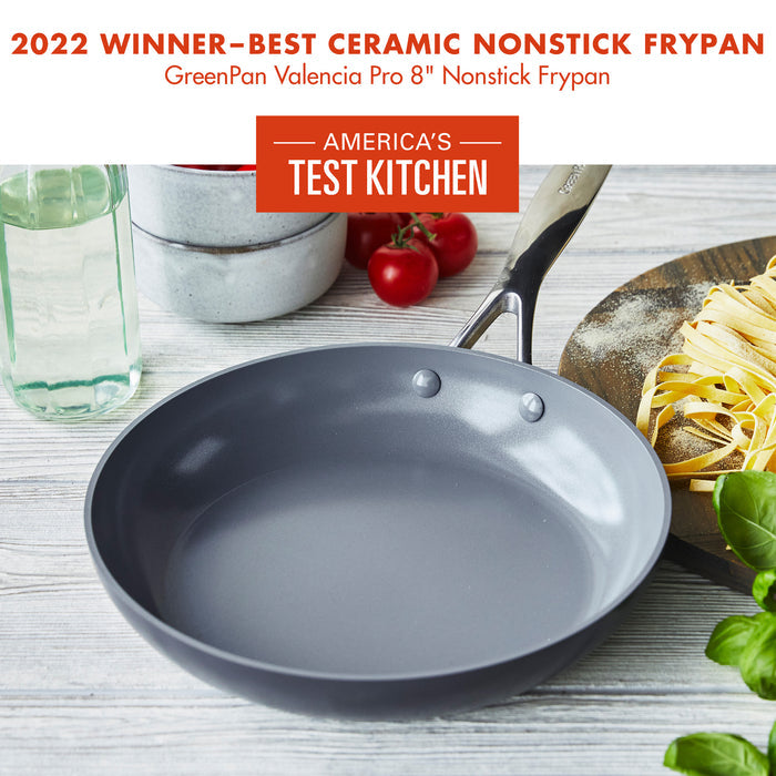 A Grey 8-inch GreenPan Valencia Pro nonstick frypan is displayed on a wooden surface, surrounded by a bottle of oil, tomatoes, and freshly made pasta. The image includes text stating it won the 2022 America's Test Kitchen award for Best Ceramic Nonstick Frypan.