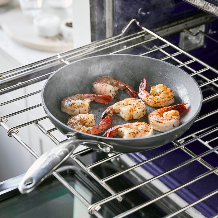 The GreenPan Valencia Pro Ceramic Nonstick Hard Anodized Fry Pan, 10, holds sizzling prawns seasoned with herbs on an open oven rack. Steam rises gracefully against a blurred kitchen backdrop, creating a cozy ambiance.