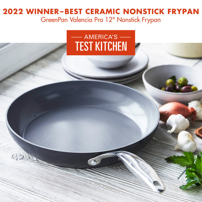 A GreenPan Valencia Pro 12" Nonstick Frypan is placed on a rustic wooden table. It is surrounded by ingredients like garlic, vinegar, and herbs. A label reads "2022 Winner - Best Ceramic Nonstick Frypan" and "America's Test Kitchen.