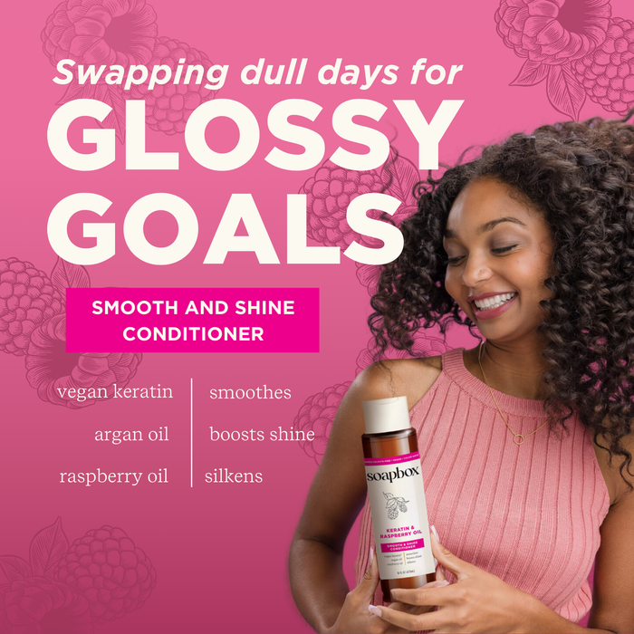 A woman with curly hair smiles, holding a bottle of Soapbox Vegan Keratin & Raspberry Seed Oil Smoothing Conditioner. The pink background says Swapping dull days for glossy goals and features key ingredients like vegan keratin, shine-boosting argan oil, and raspberry seed oil.