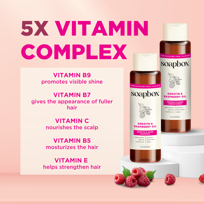 A pink and white graphic displays two Soapbox Vegan Keratin & Raspberry Seed Oil Smoothing Conditioner bottles on a podium, highlighting a 5X Vitamin Complex with shine-enhancing argan oil and benefits from Vitamins B9, B7, C, B5, E. Raspberries are scattered around the base.
