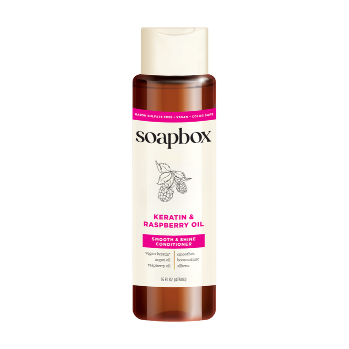 A 16 fl oz (473 ml) bottle of Soapbox Vegan Keratin & Raspberry Seed Oil Smoothing Conditioner is infused with vegan keratin, sulfate-free, color-safe, and enriched with shine-boosting argan oil.