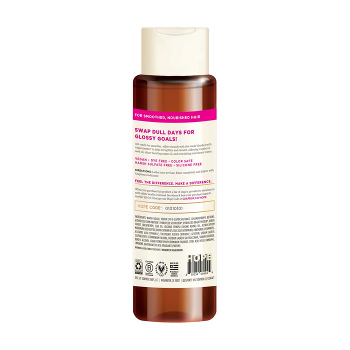 The Soapbox Vegan Keratin & Raspberry Seed Oil Smoothing Shampoo features a pink label and white cap, offering benefits like a 5X vitamin complex and color-safe vegan keratin. Ingredients are listed at the bottom with a barcode, completing its sleek design.