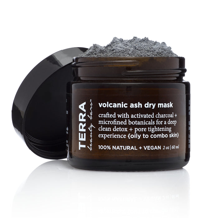 An open dark brown Terra Beauty Bars jar labeled Volcanic Ash Dry Facial Clay Mask reveals gray powder. This vegan formula uses activated charcoal for deep cleansing and pore tightening.