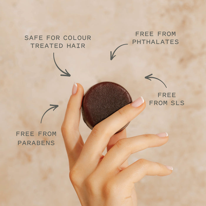 A hand holds the Good Juju Body & Home Volumizing Conditioner Bar for Oily/Fine Hair against a beige background. Text: Safe for colour-treated hair, free from phthalates, SLS, and parabens—ideal for natural hair care.