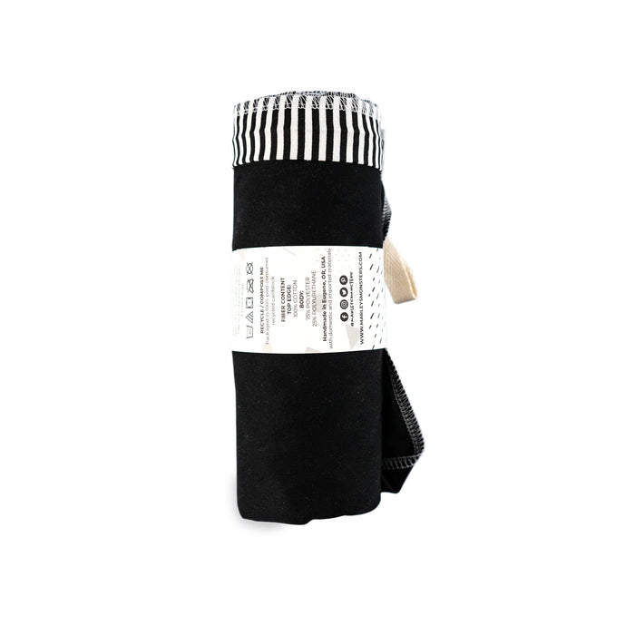 The Washable Trash & Recycling Bag by Marleys Monsters features a rolled-up black design with a white label showcasing text and symbols. It has stylish black and white stripes on the top edge, is made from water-resistant fabric, and secured with a durable black strap for easy transport.
