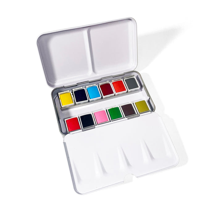 The Elseware Unplug Watercolor Set includes 12 vibrant rectangular paints arranged in two rows inside a white travel case, with mixing palettes on the lid and base for convenient painting on the go.