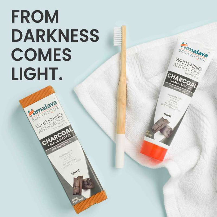 A charcoal toothpaste and toothbrush lie on a white towel against a light blue background. Text reads "FROM DARKNESS COMES LIGHT." The toothpaste packaging highlights charcoal, black seed oil, and mint as ingredients.