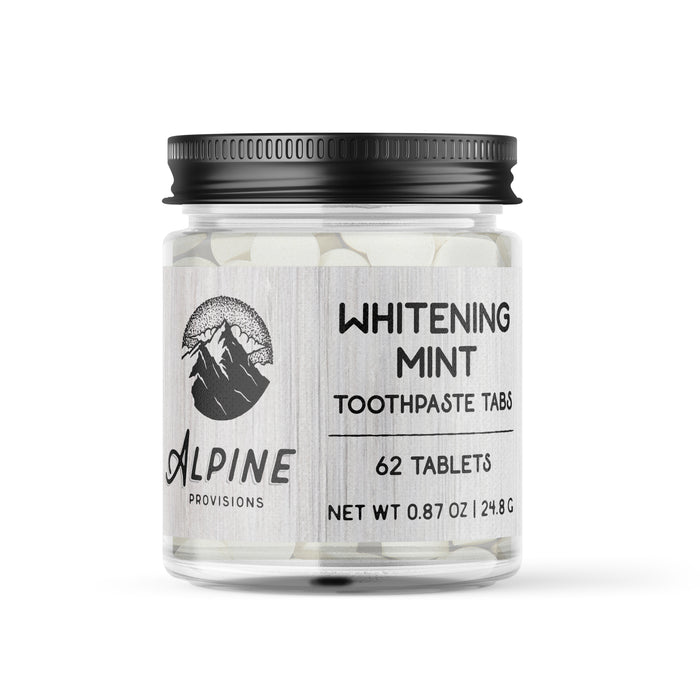 A clear jar with a black lid contains 62 Alpine Provisions Whitening Mint Toothpaste Tabs. The label, featuring a mountain logo, reads Whitening Mint Toothpaste Tabs. Great for healthy teeth and gums, these tabs aid in preventing plaque buildup. Net weight: 0.87 oz / 24.8 g.