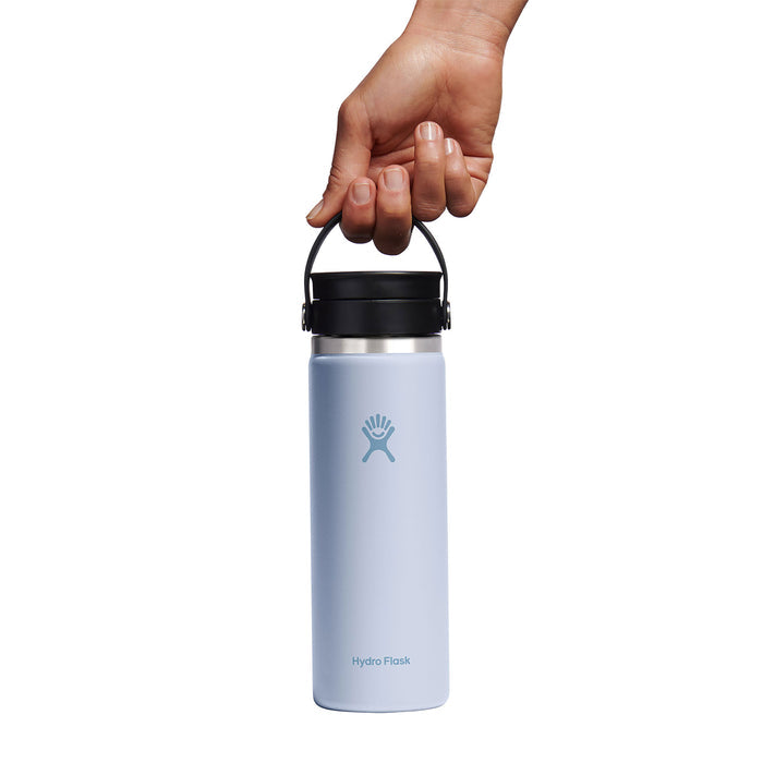 A hand holds a Hydro Flask Wide Mouth Bottle with Flex Sip Lid™ in light blue, 20 oz of insulated stainless steel, black cap with handle, against a white backdrop. Featuring TempShield double-wall insulation for peak performance.