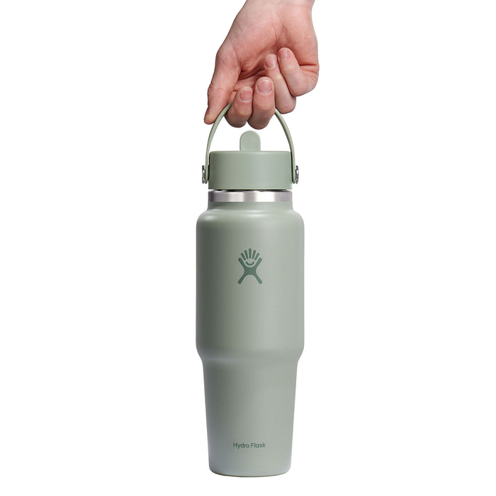 A hand holds a 32 oz Hydro Flask Wide Mouth Travel Bottle with Flex Straw Cap, featuring the brands logo and text at the base, designed to be leakproof against a plain white background.