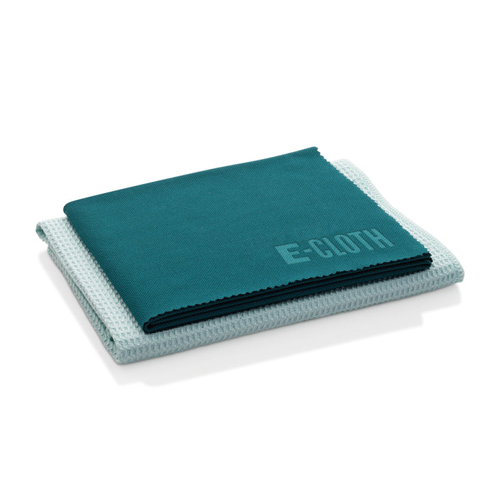 Two folded cloths are stacked: the top is a dark teal microfiber with E-Cloth embossed; below is a light blue textured one, ideal for streak-free window cleaning. The background is white. Brand: E-Cloth. Product: Window Cleaning Kit.