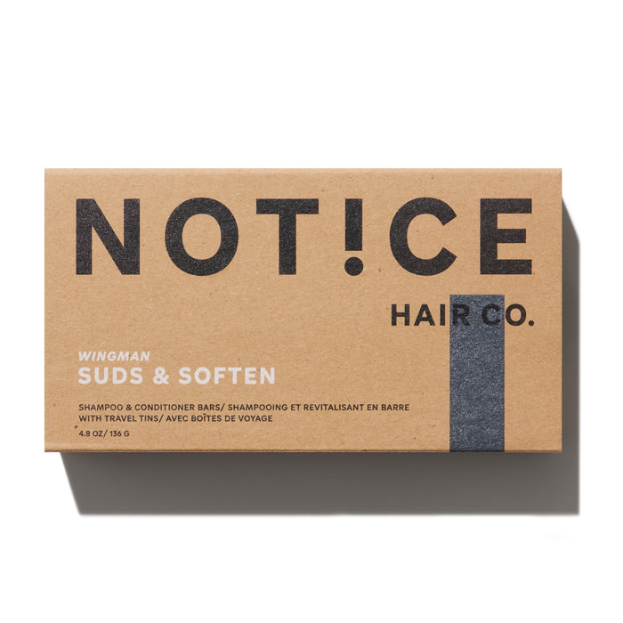 A NOT!CE Hair Co. brown box with black lettering contains the Wingman Travel Set—Wingman Suds & Soften bars infused with essential oils to boost hair growth. These shampoo and conditioner bars, weighing 4.8 oz/136 g, include travel tins for sustainable self-care on the go.