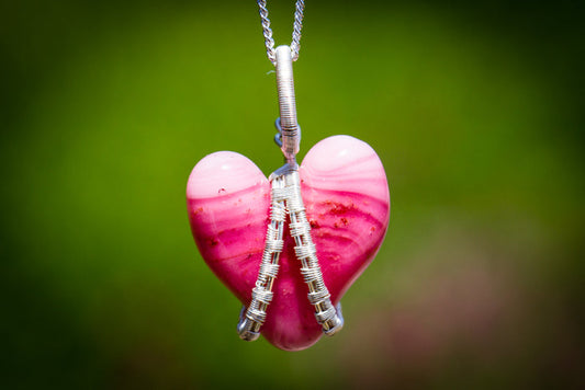 Pink glass heart pendant wrapped in silver wire hanging from a silver chain.
