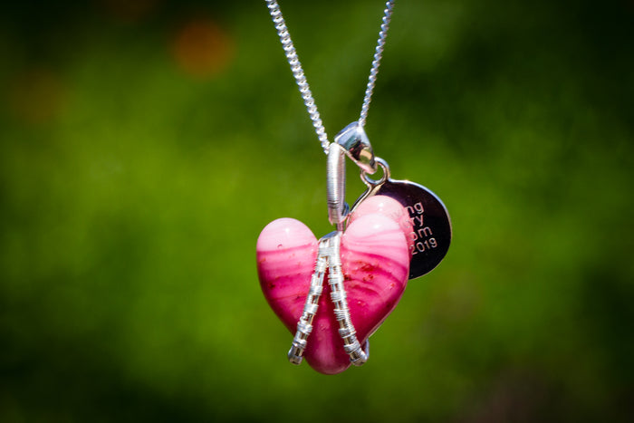 Pink glass heart pendant wrapped in silver wire with a round engraved memorial tag on a silver chain.