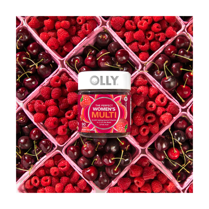 A bottle of OLLY Womens Multi gummy vitamins is surrounded by a grid of fresh raspberries and cherries in square baskets, with the vibrant reds offering a contrasting backdrop to highlight the essential B Vitamins in this womens multivitamin.