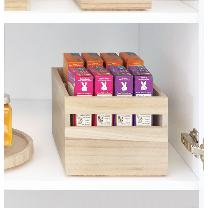 An iDesign Wood Handled Bin on a white shelf holds six small soap boxes in two rows, featuring orange and purple boxes with the leaping bunny logo. To the left, a small round container with a yellow substance complements this versatile organizer.
