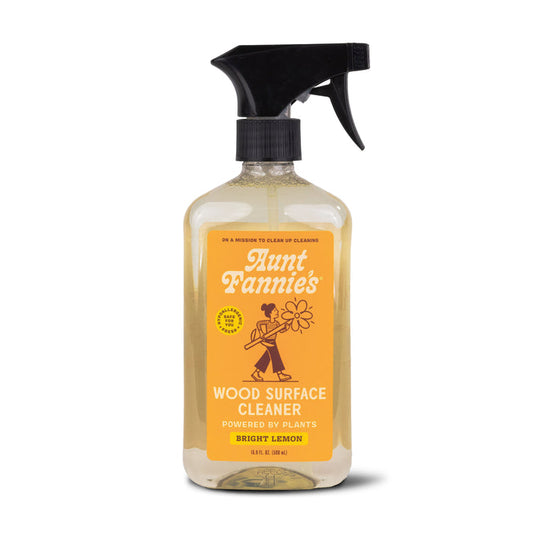 Aunt Fannies Wood Surface Cleaner comes in a spray bottle with bright lemon scent and essential oils. The label, featuring a person and flower, emphasizes plant-powered surfactants, while the bottle contains clear liquid.
