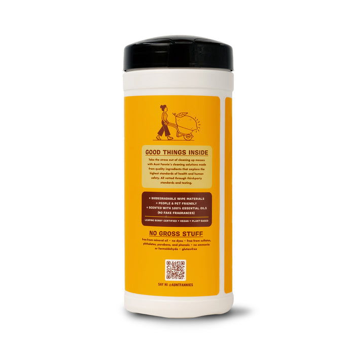 A sleek white cylindrical container with a black lid, labeled in yellow with an illustration of a person pushing a cart, showcases Aunt Fannies Wood Surface Wipes. The natural formula features essential oils and is paraben-free.