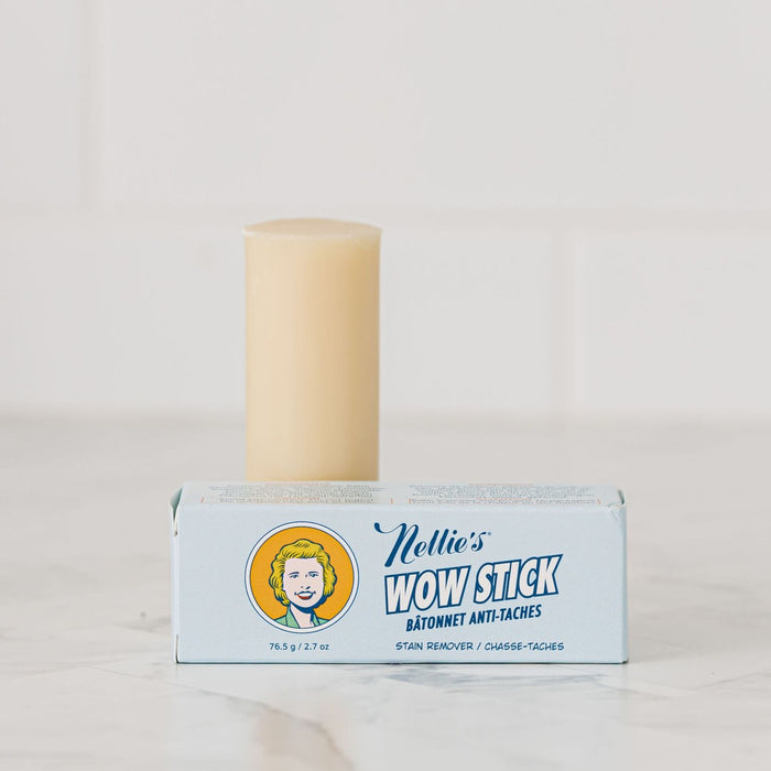 A beige WOW Stick Stain Remover stands behind its light blue Nellie’s box on a white surface with a tiled background, highlighting this natural stain remover as an essential green cleaning product.