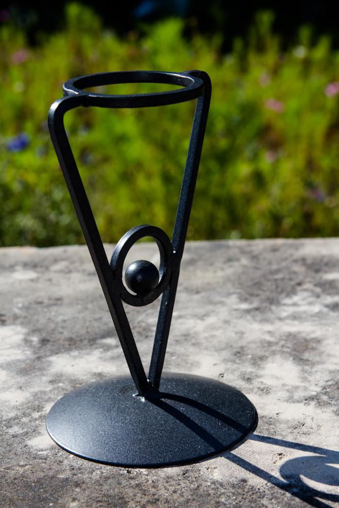 Close-up of black triangle iron stand with orb, shown on a textured outdoor surface