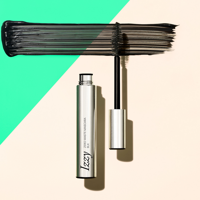 A tube of IZZY Zero Waste Beauty’s Zero Waste Mascara, wand removed, rests on a beige and mint green diagonal background. Its black color and texture are displayed in a swipe above the wand, highlighting this sustainable beauty essential.