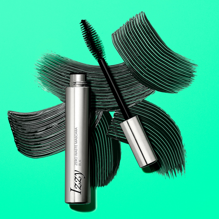 A silver tube of IZZY Zero Waste Beautys Zero Waste Mascara with its wand out rests on a bright green background, bold black mascara swipes behind it, showcasing a dedication to sustainable beauty.