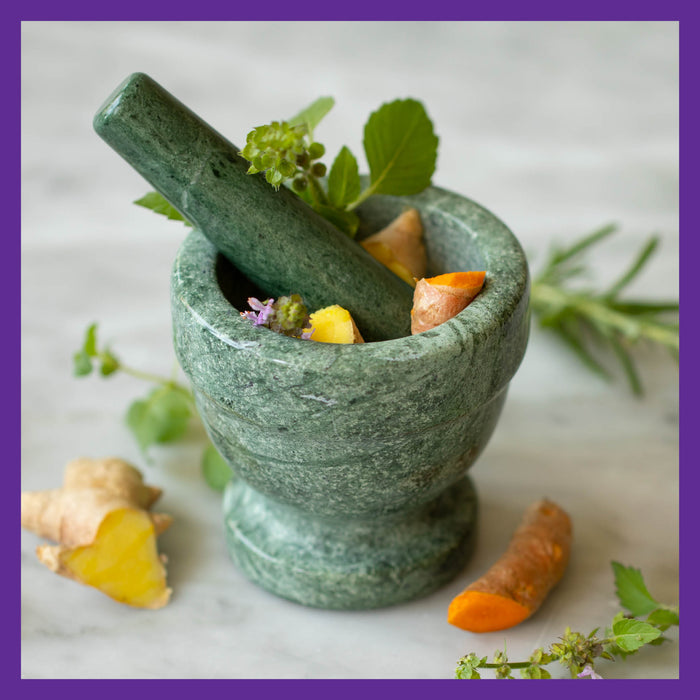A green marble mortar and pestle filled with turmeric and ginger roots, known for inflammation relief, sits on marble. Fresh herbs add greenery. A purple border frames the image, highlighting New Chapters Zyflamend™ Herbal Pain Relief for healthy inflammation and joint support.